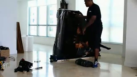 mover stretch-wrapping a grand piano stood on its side in a high-rise condo