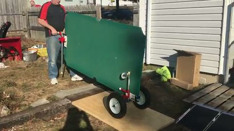 man wheeling a one-piece pool table slate on a dolly across a backyard